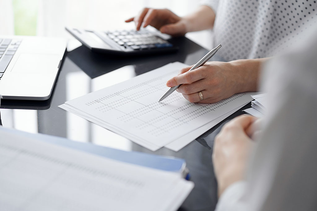 Woman Accountant Using A Calculator And Laptop Computer While Counting Taxes For A Client. Business Audit And Finance Concepts